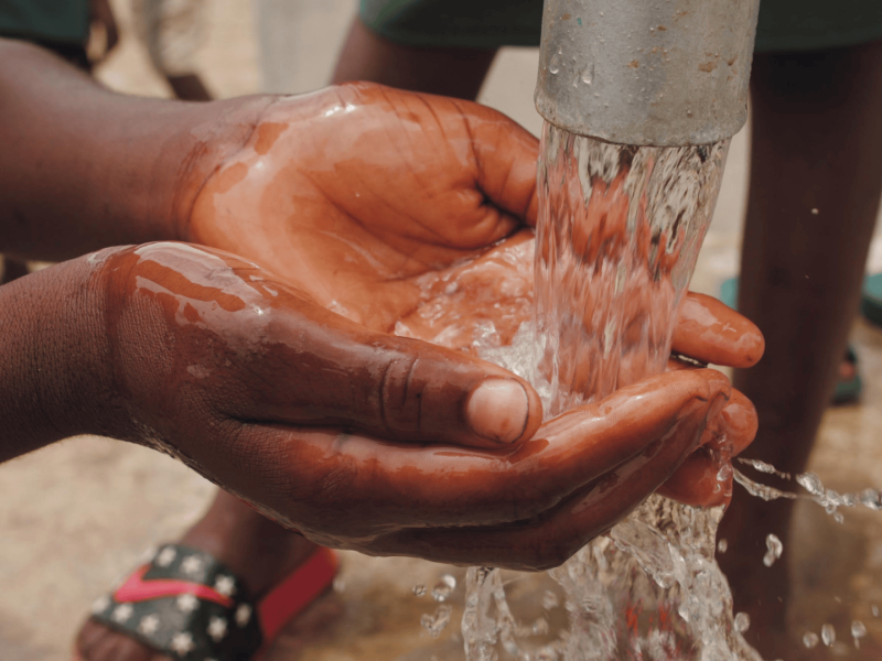 Child's hand below a water pump